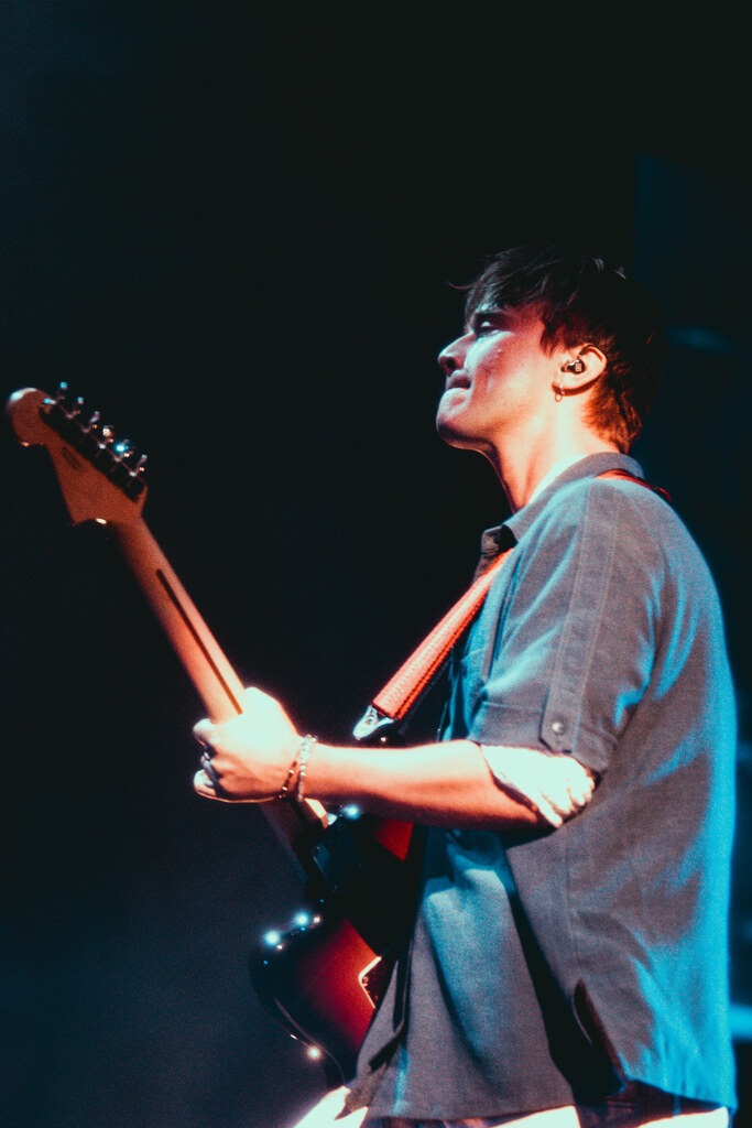 A Balu Brigada guitarist performs beneath blue stage lighting.