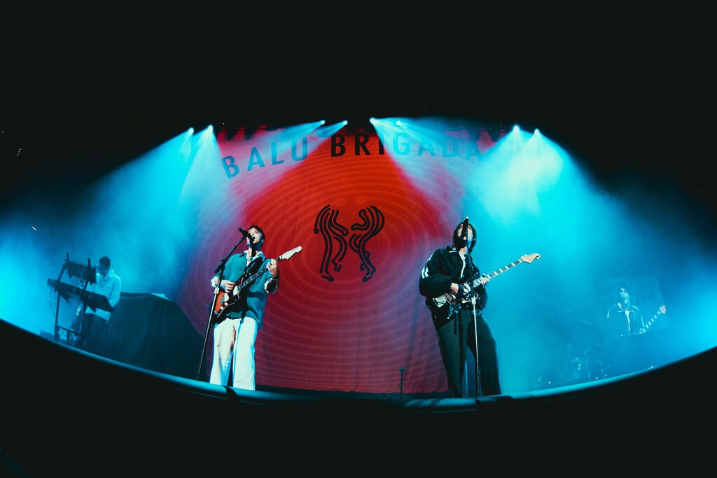 Balu Brigada perform in front of their red stage backdrop beneath blue lights.