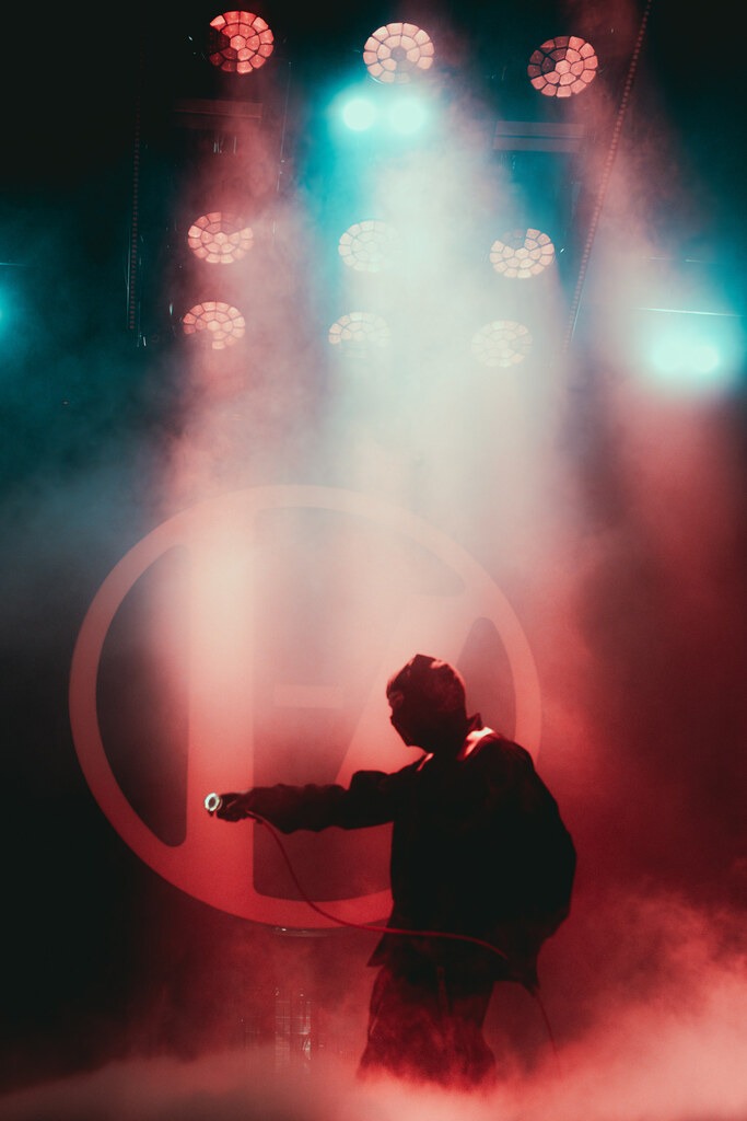 A performer stands in blue and red stage haze with one arm extended.