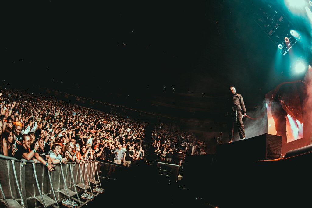 Wide view of the arena crowd and a performer on stage under blue and orange lights.