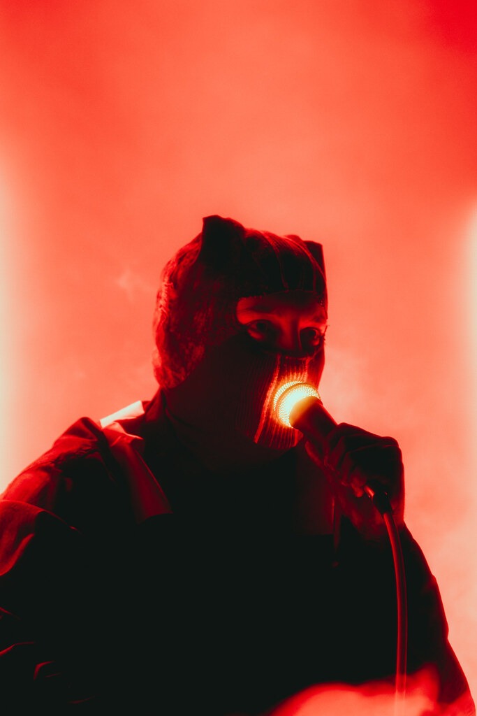 A masked Twenty One Pilots singer performs in red stage lighting.